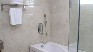 A modern bathroom with a glass-enclosed shower, a white bathtub, and a marble-tiled wall.