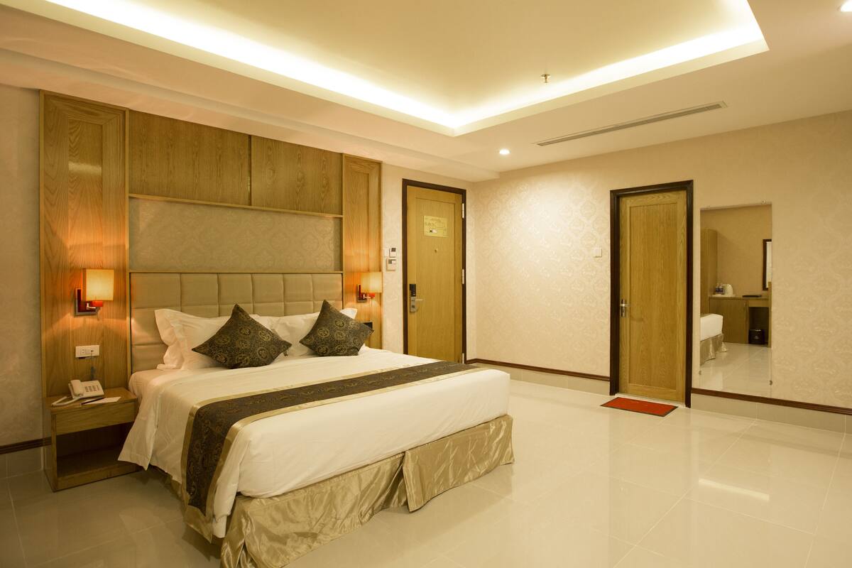 A modern hotel room with a large bed, bedside lamps, a wooden headboard, and a mirror on the wall.