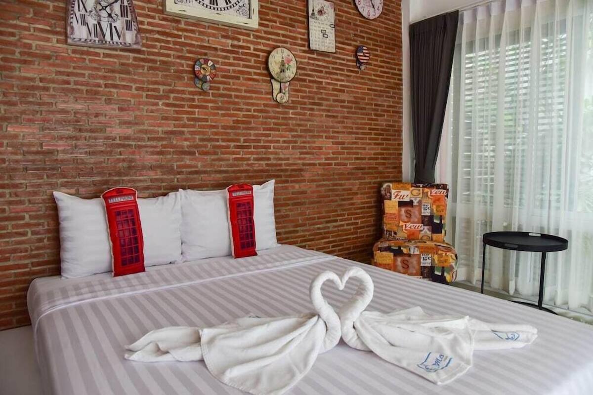 Hotelkamer met een bakstenen muur, een bed met witte lakens, een handdoek in de vorm van een hart en een raam met gordijnen.