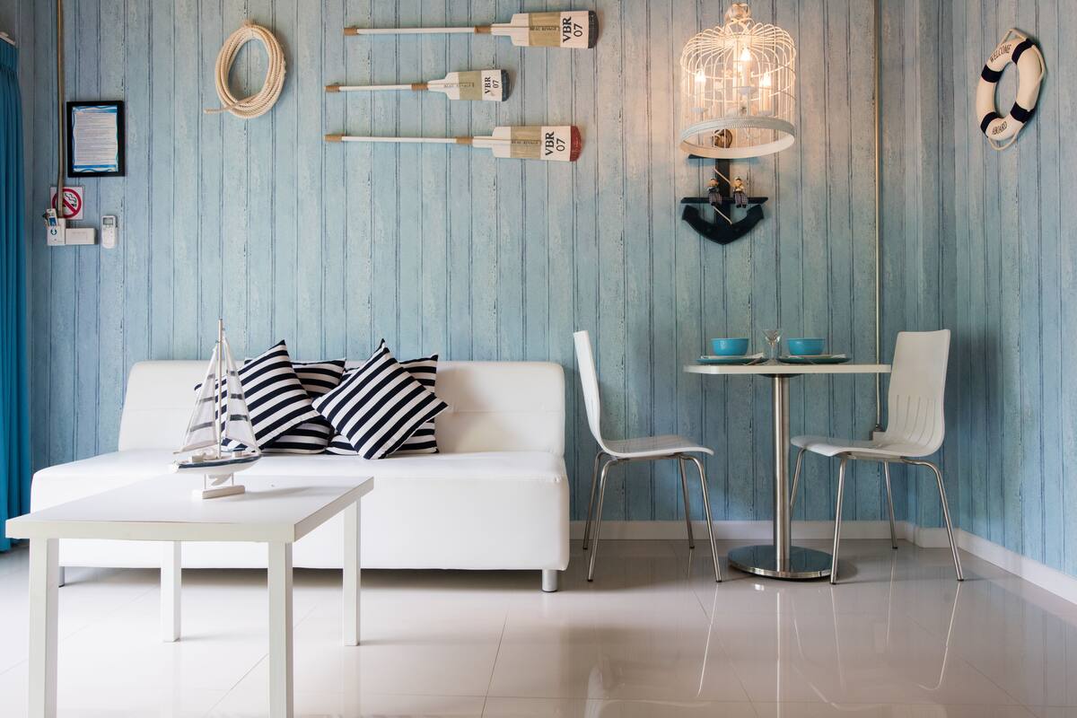 Een kamer met een witte bank, een klein rond tafeltje en twee witte stoelen. Er zitten wandlampen en een reddingsboei aan de muur.
