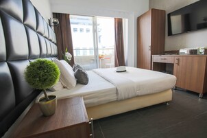 Habitación de hotel moderna con una cama grande, una planta pequeña en maceta, un escritorio y un televisor.