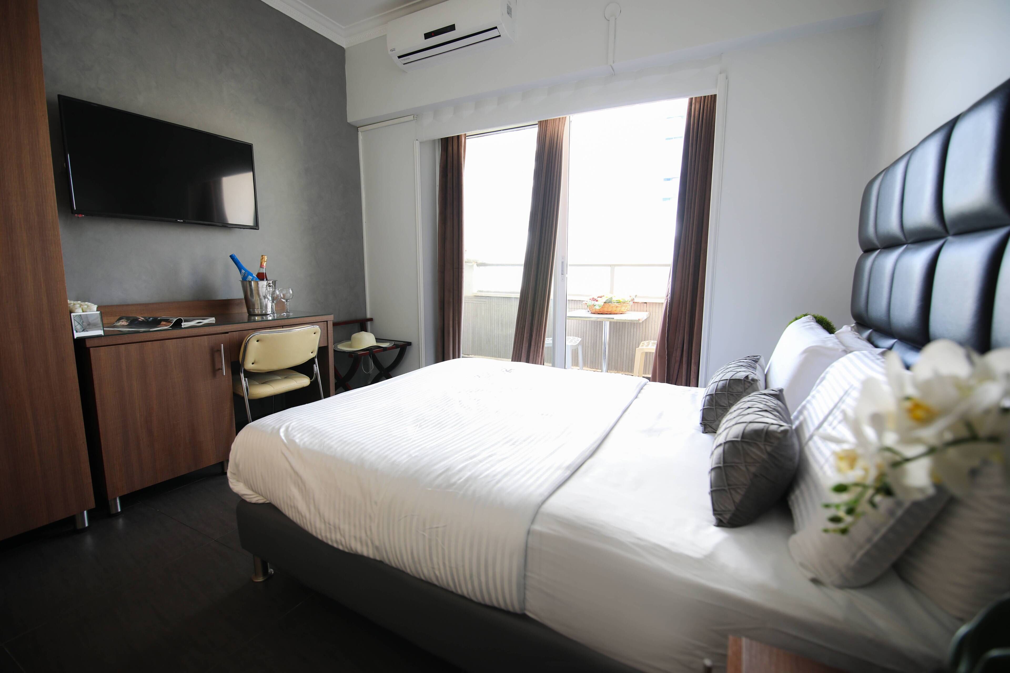 Une chambre d’hôtel avec un lit, un bureau, une chaise, une télévision et un balcon avec des rideaux.