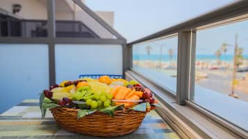 A wicker fruit basket on a table by a window overlooking a beach.