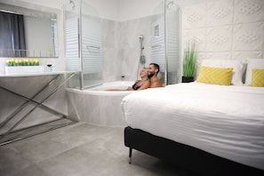A modern bathroom with a glass-enclosed shower, a bathtub, and a vanity with a mirror and toiletries. - Miami Beach Hotel Tel Aviv (Tel Aviv)