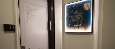 A door with a decorative panel, a framed artwork of deer and a tree, and two potted plants on a shelf.