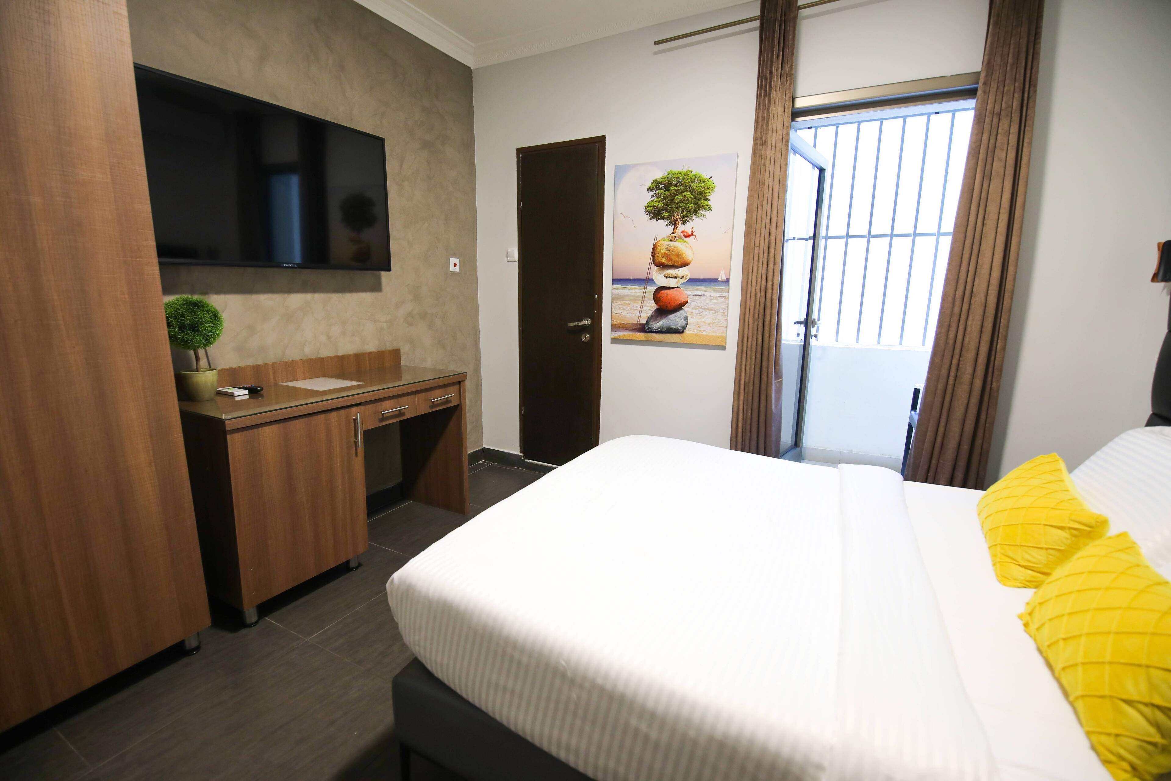 Ein Hotelzimmer mit Bett, Schreibtisch, Fernseher und einer Tür zum Balkon.