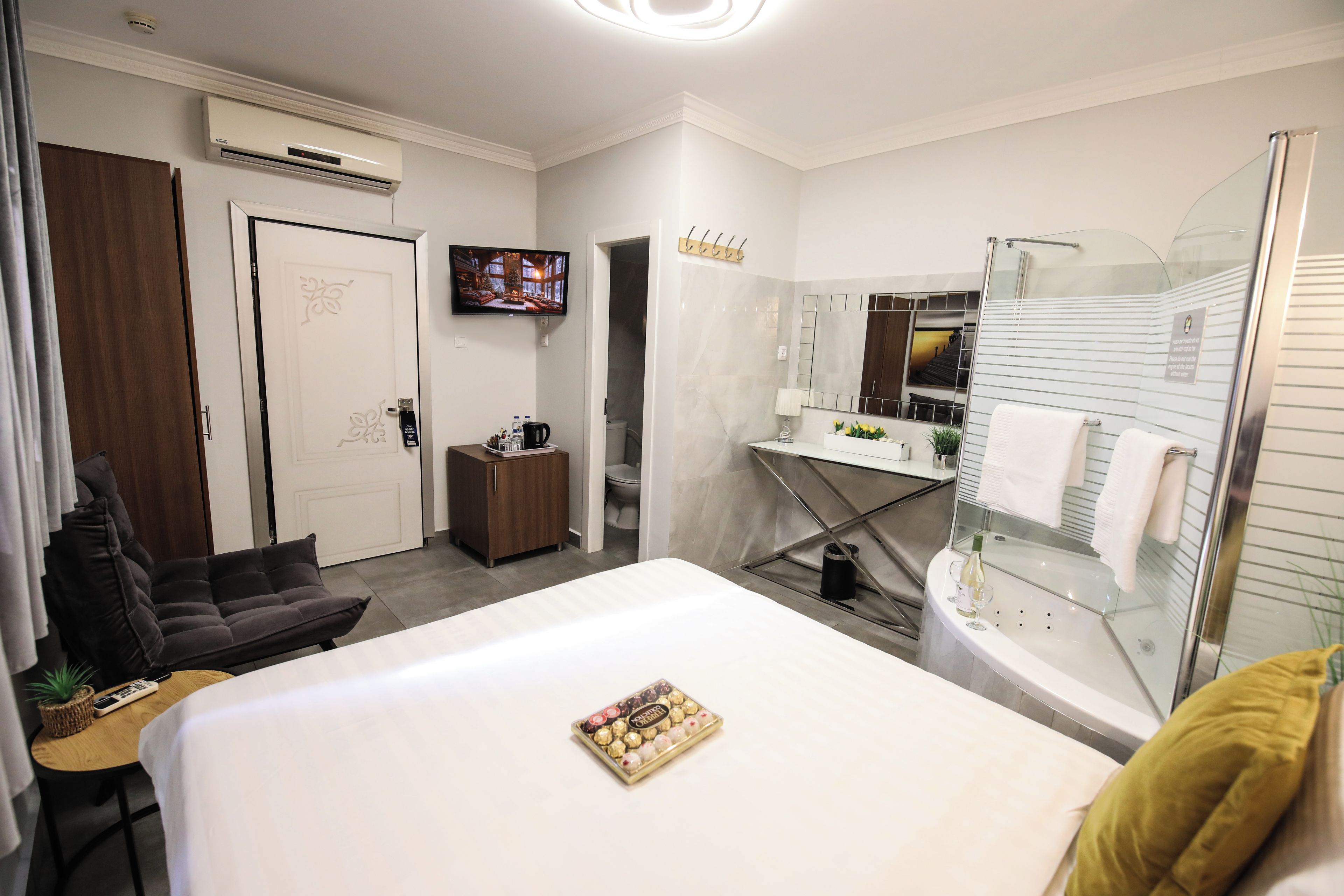 A hotel room with a bed, a TV, a small cabinet, a bathroom with a mirror, and a shower area.