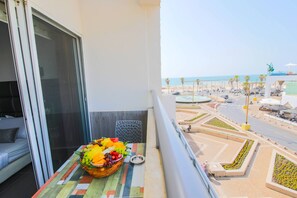 Enjoy breathtaking views of the beach and city from this room's balcony, featuring a table with a fruit basket and a small plate.