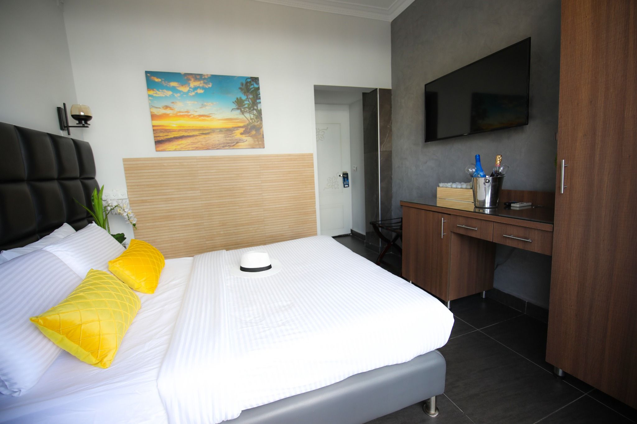 A hotel room with a bed, a desk, a television, and a painting on the wall.