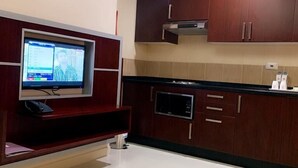 A modern kitchen with dark wooden cabinets, a built-in microwave, and a flat-screen TV mounted on a wooden shelf. - Hala Inn Hotel Apartments (Ajman)