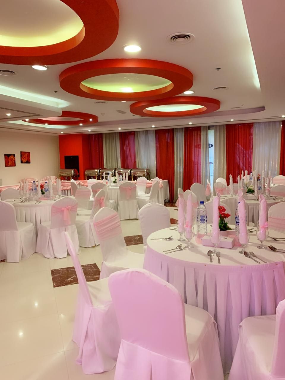 A banquet hall with round tables, white chairs, and red curtains.