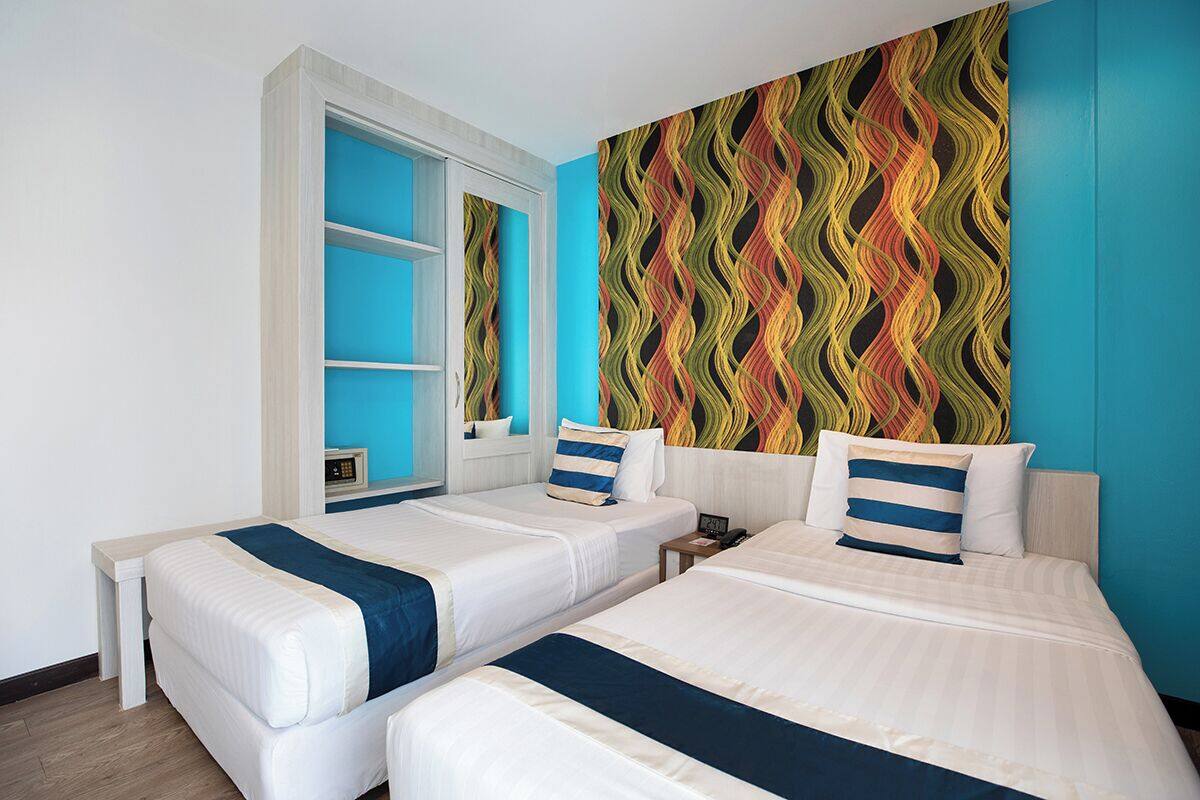 Ein Hotelzimmer mit zwei Betten, einem großen Fenster und einem farbenfrohen Wandmuster.