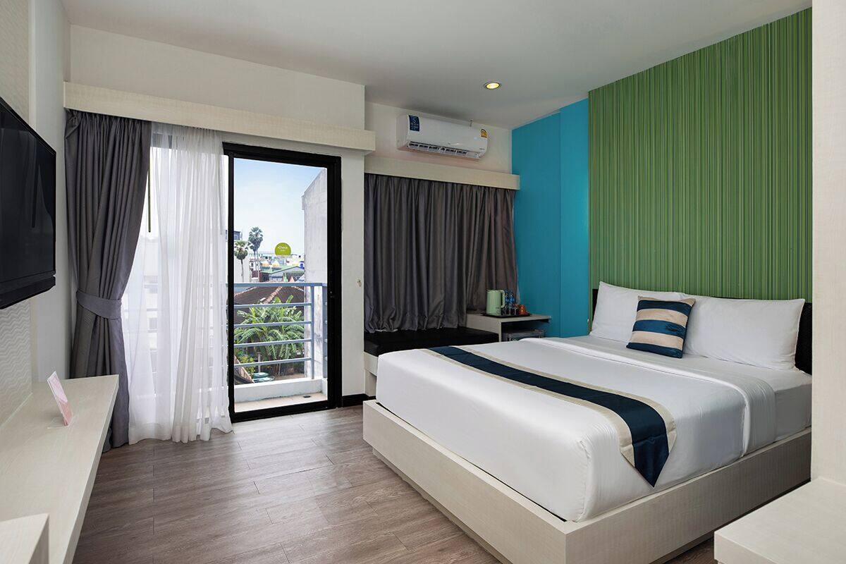 Ein Hotelzimmer mit einem großen Bett, einem Schreibtisch und einem Balkon mit Blick auf Palmen.