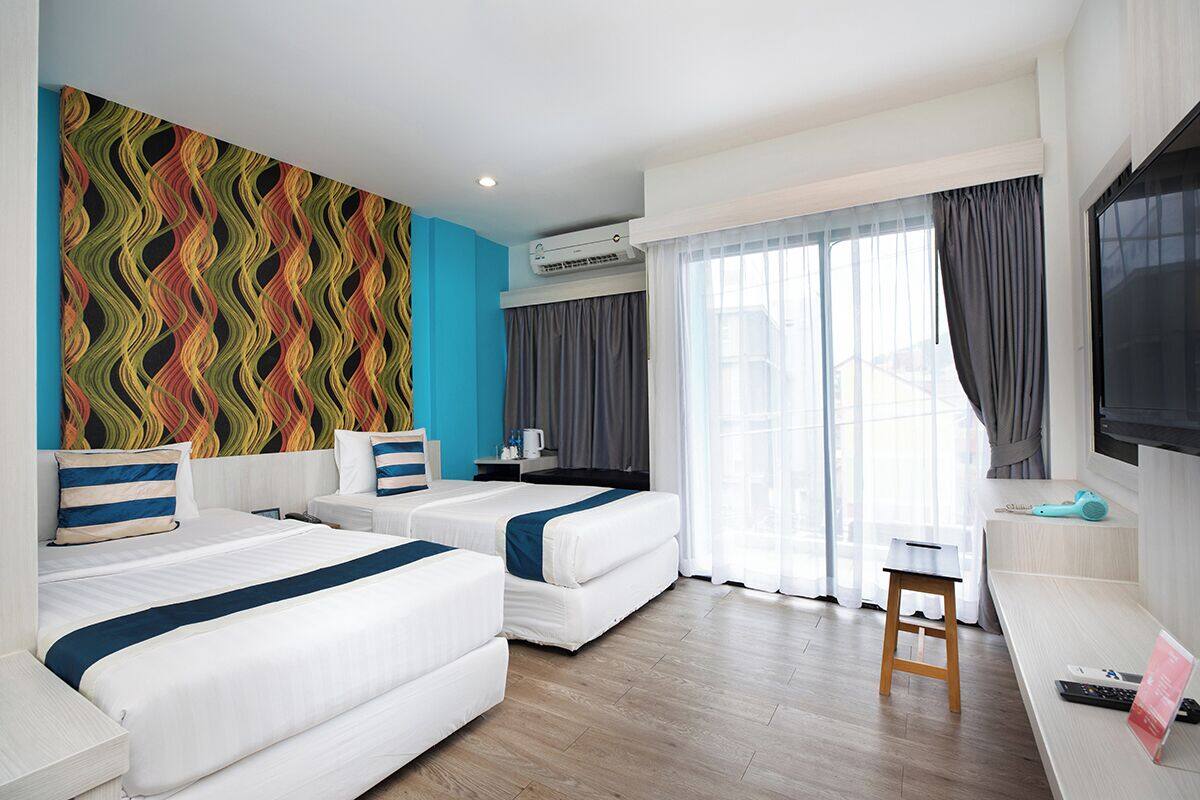 Ein Hotelzimmer mit zwei Betten, einem Fernseher, einem Schreibtisch und einem Fenster mit Vorhängen.