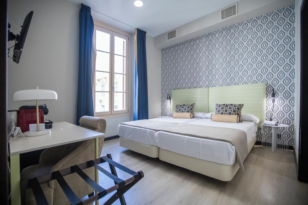 A double bed with patterned headboard, a desk with a lamp, and a chair.