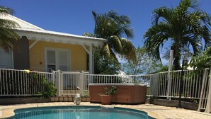 A clear blue swimming pool with a tiled deck, surrounded by a white fence and palm trees. - Résidence Bel'Bay (Les Anses-d'Arlets)