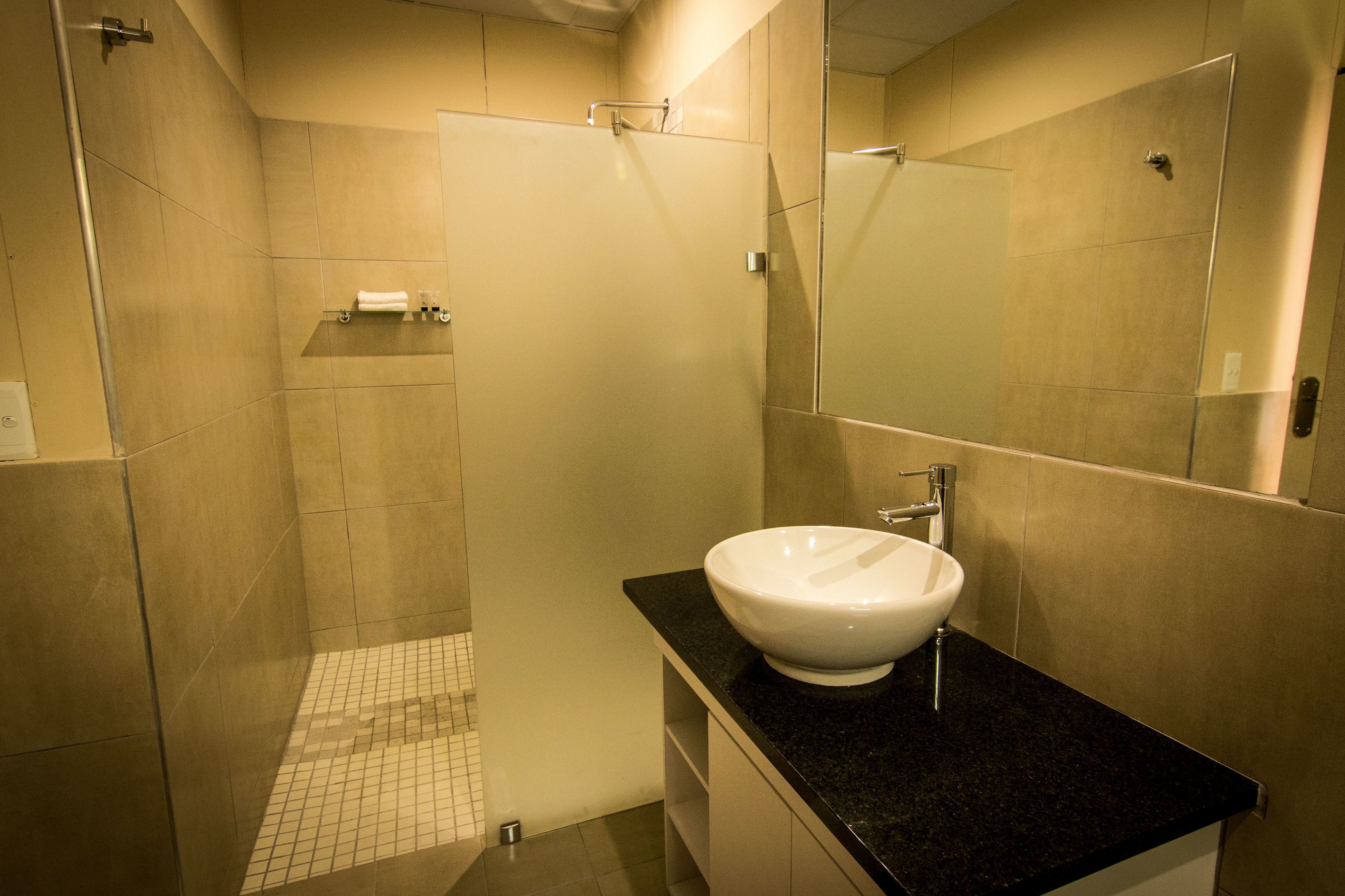 A modern bathroom with a large mirror, a white sink, and a shower area.