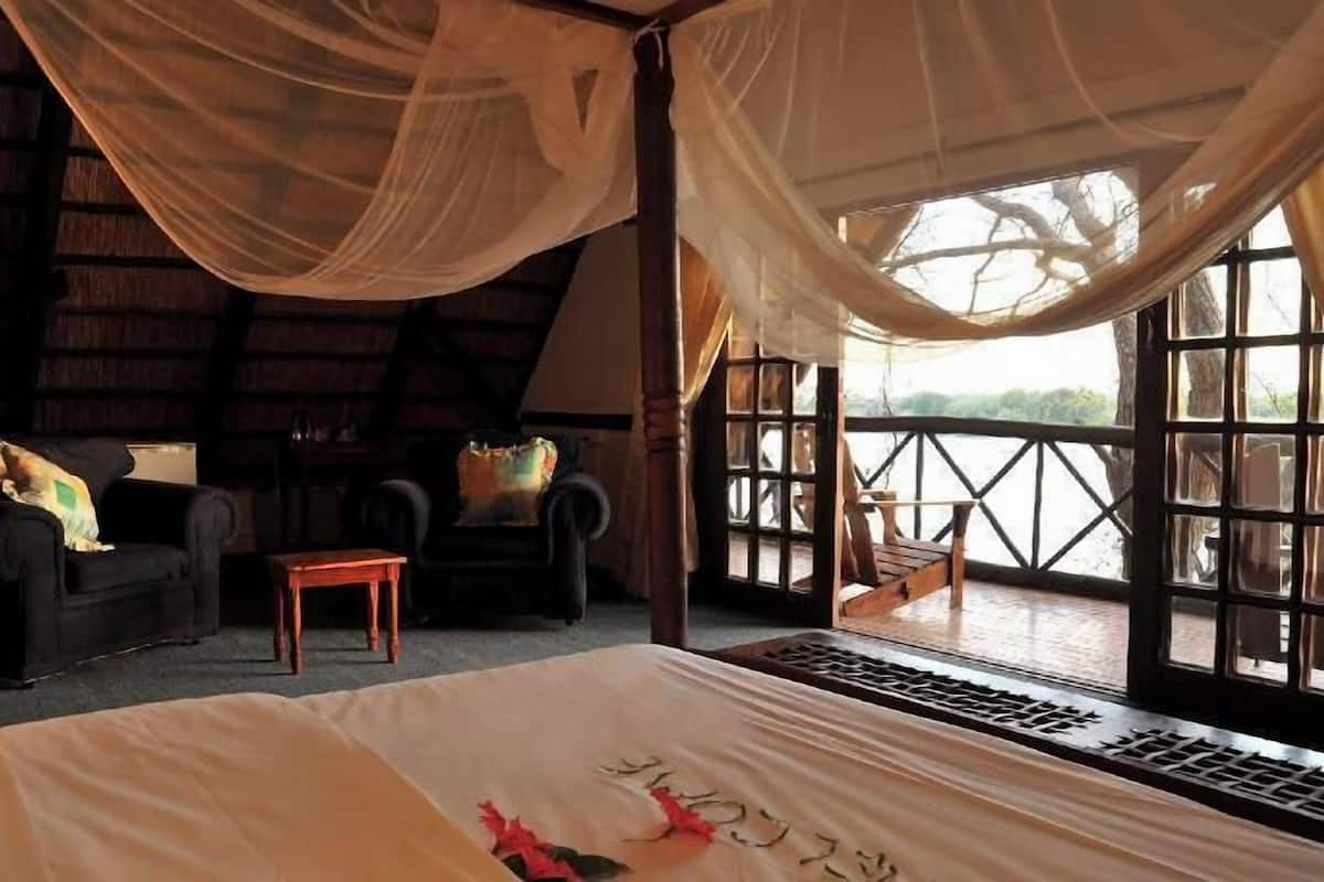 A room with a bed, a chair, a small table, and a balcony with a railing.