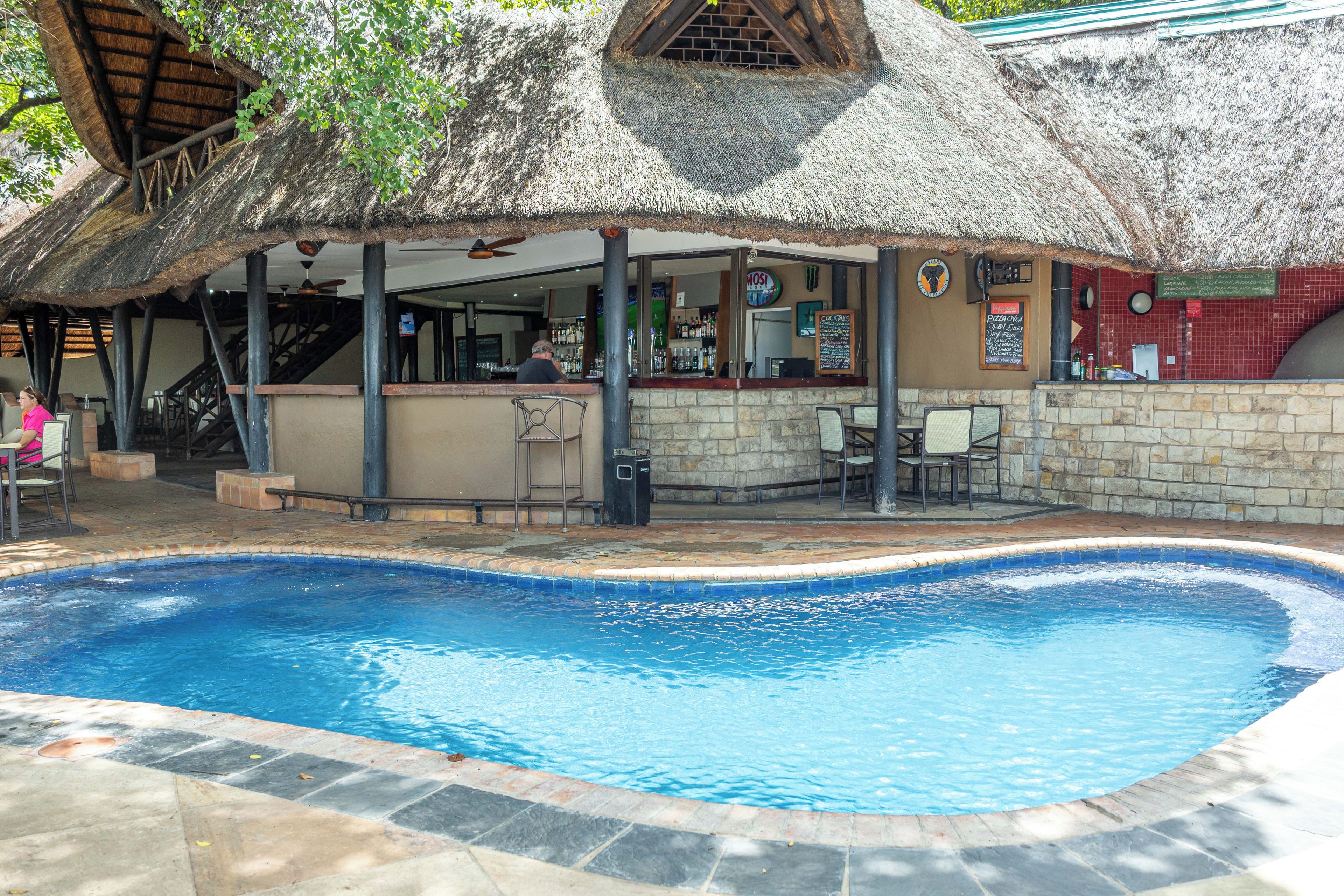 A pool area with a bar and seating under a thatched roof.