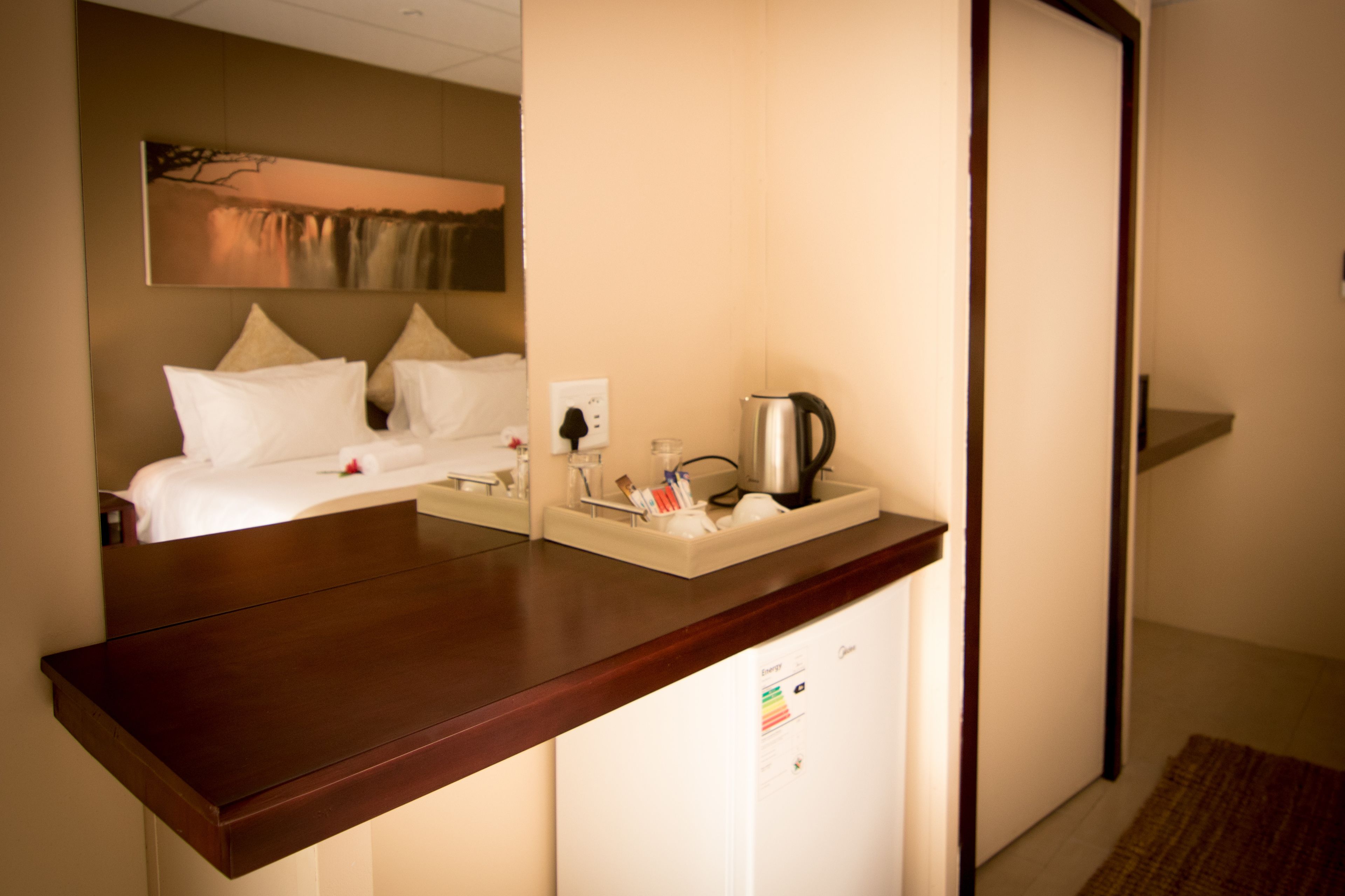 Una habitación de hotel con una cama, una mesita de noche con un hervidor y un refrigerador pequeño.