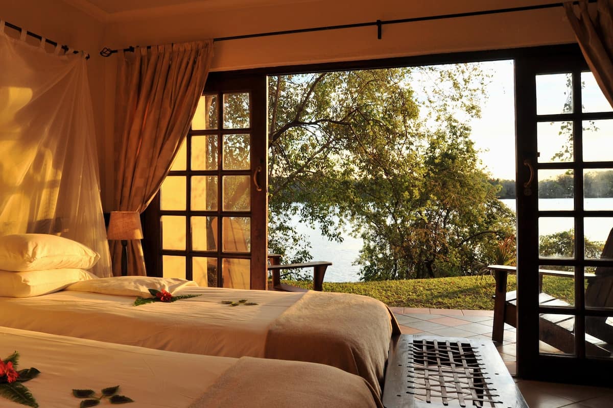 A bedroom with two beds, a view of a lake, and a chair outside.