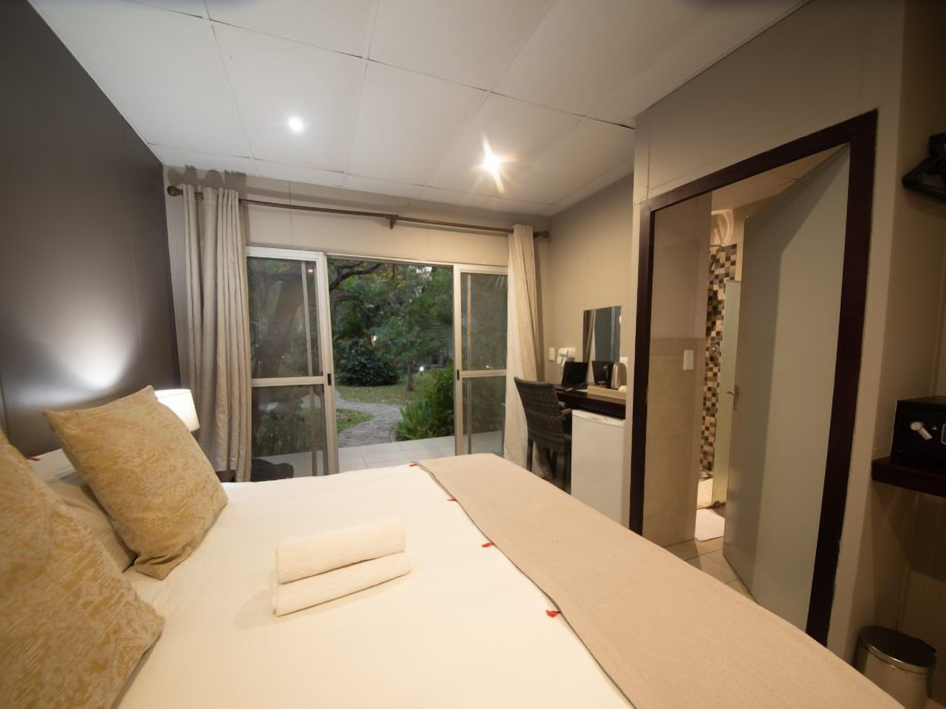 Une chambre d’hôtel avec un grand lit, un bureau équipé d’un ordinateur et une vue sur la verdure environnante.