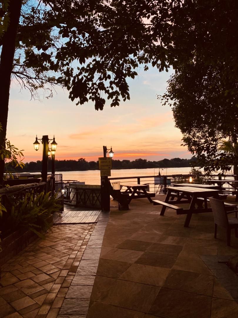 An outdoor patio area with picnic tables and a view of a body of water during sunset.