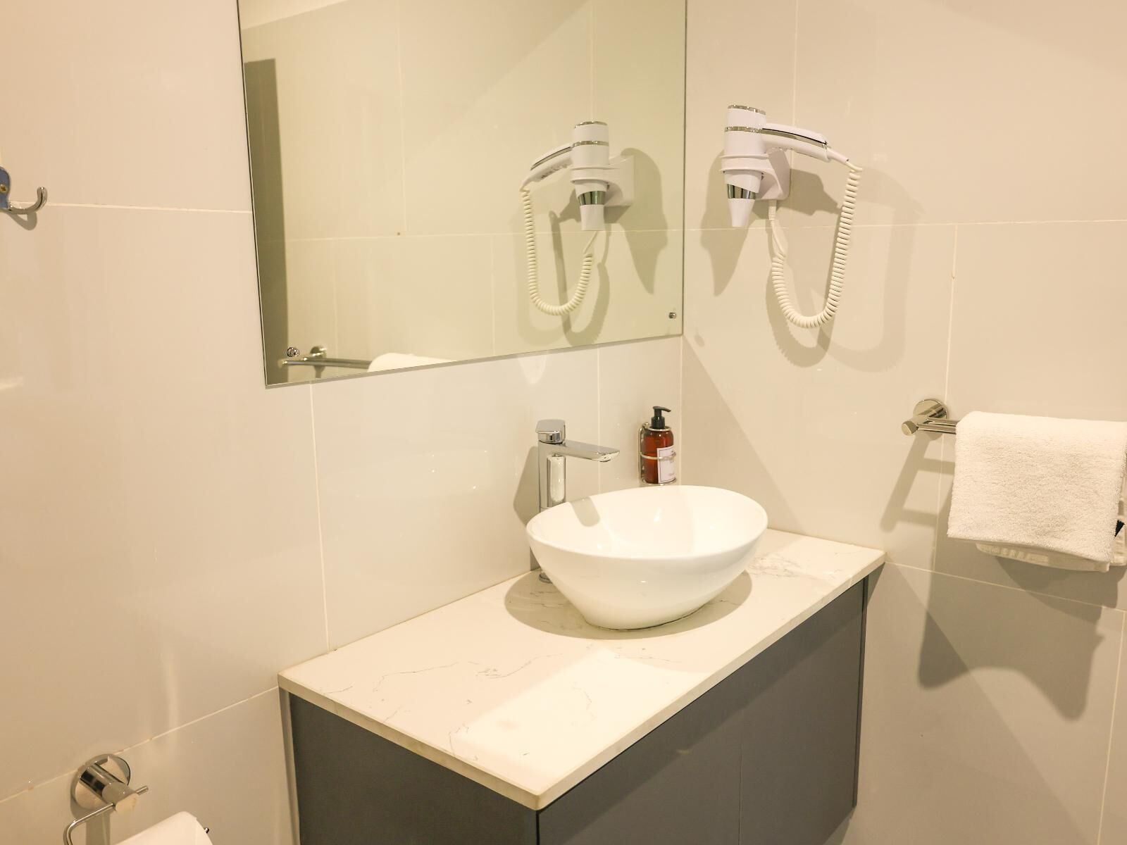 A bathroom with a white sink, a mirror, a hairdryer, and a towel rack.