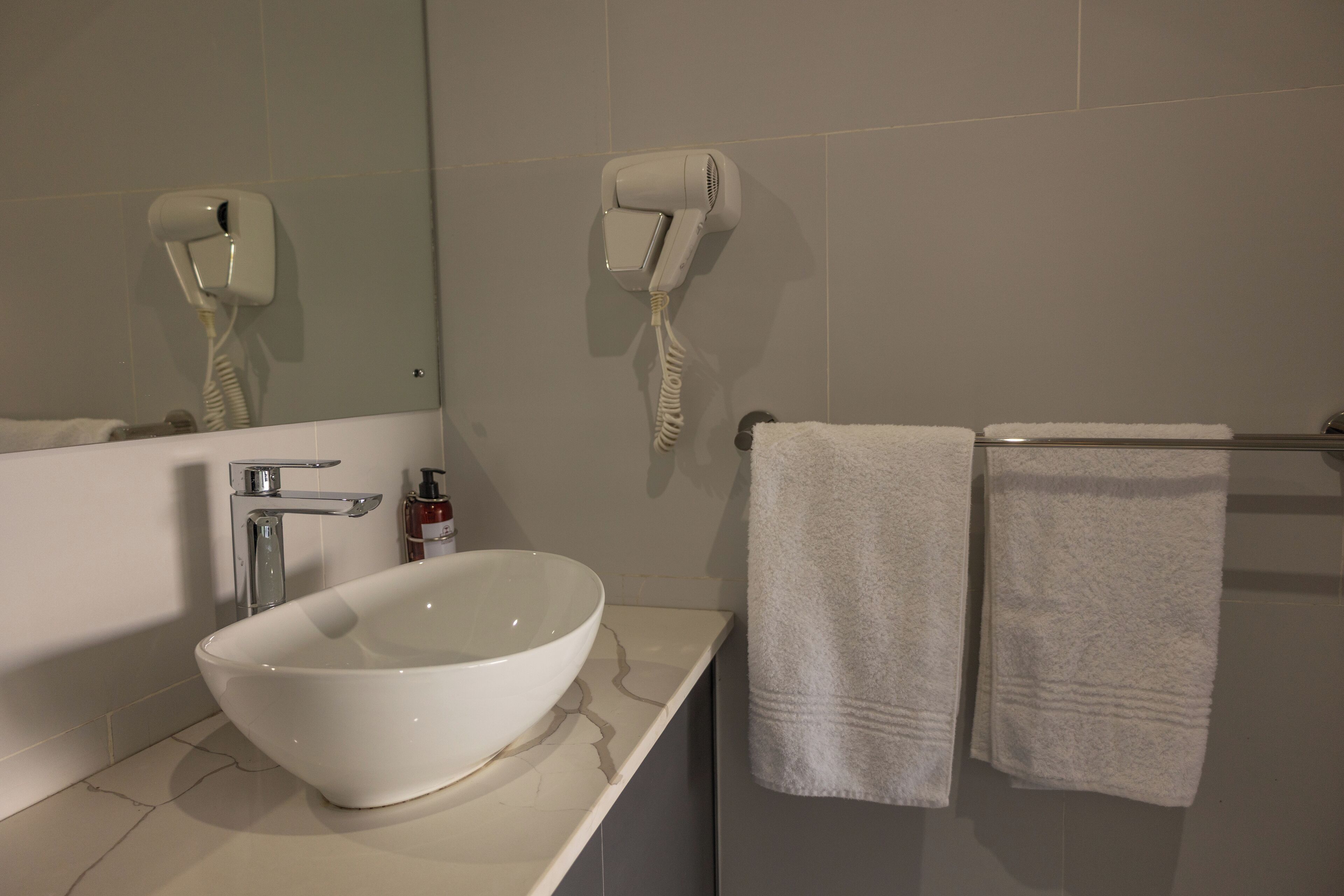 Un baño con lavamanos blanco, un espejo, un secador de pelo y dos toallas en un tendedero.