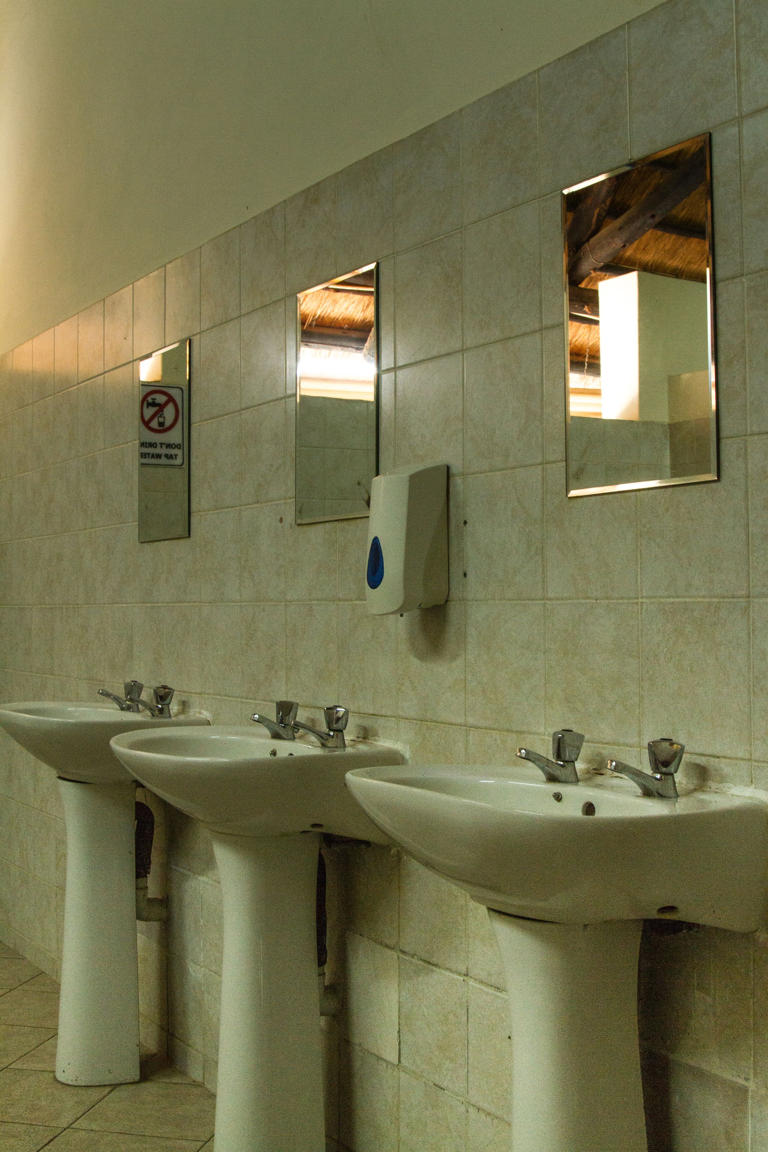 Een openbaar toilet met drie wastafels en spiegels aan de muur.