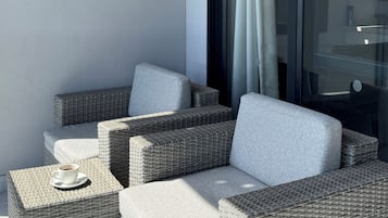 Un balcon doté de meubles en osier, notamment d’un canapé et de deux poufs carrés, ainsi qu’une porte vitrée avec un rideau.