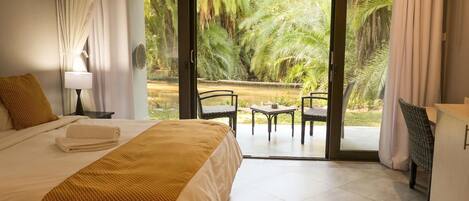 Une chambre à coucher comprenant un lit, une table de chevet, une lampe et donnant sur une terrasse extérieure avec des chaises et une table.