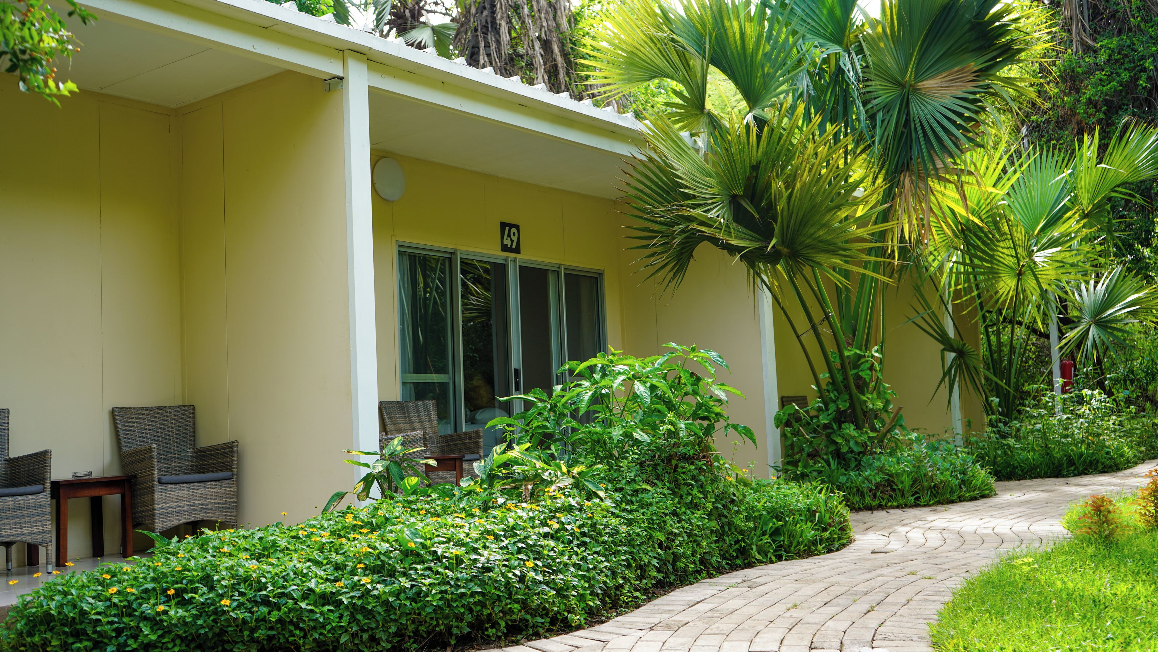 A building with a yellow exterior, a covered porch with wicker furniture, and a paved pathway.