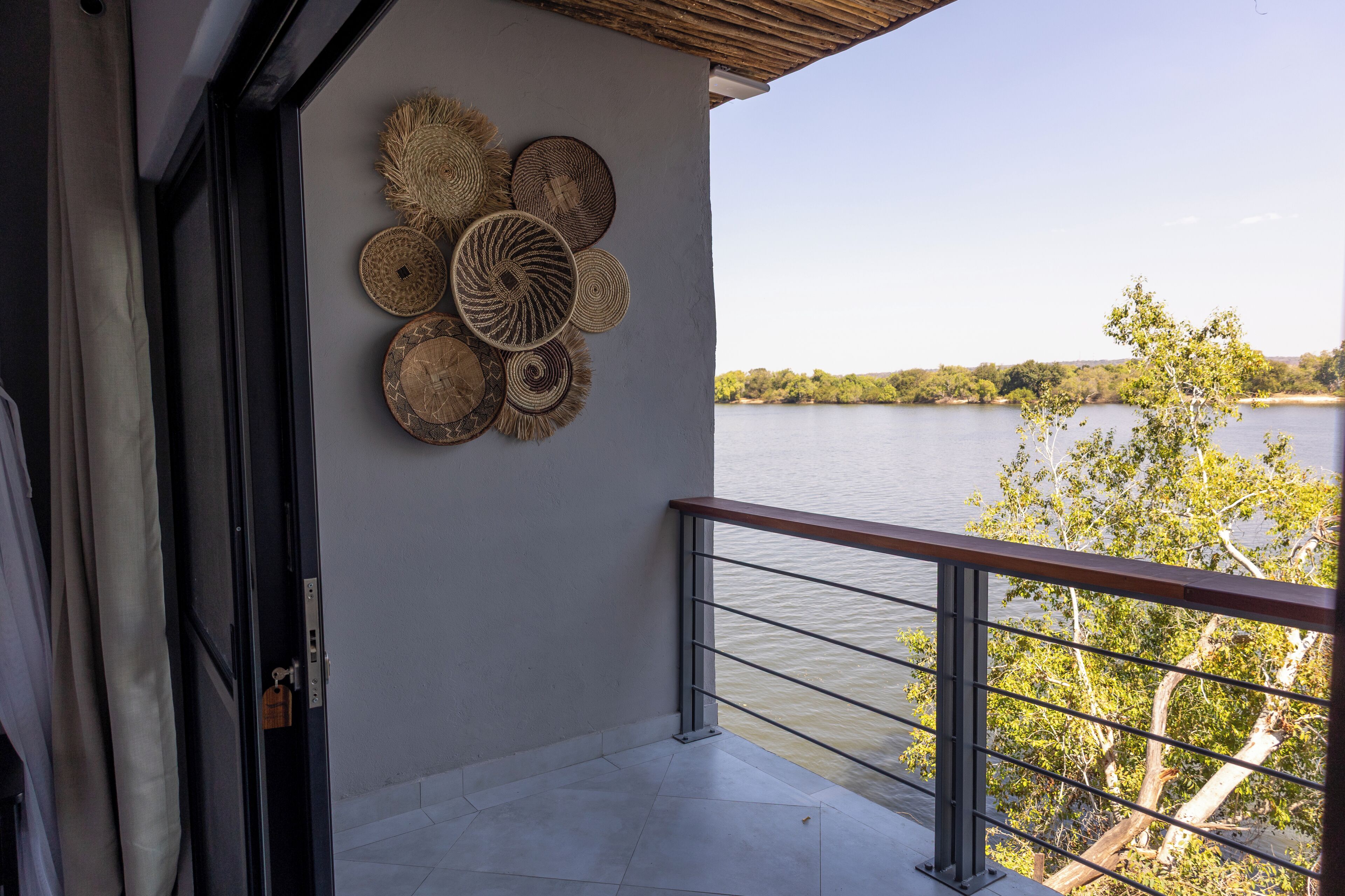 A balcony with a railing overlooking a body of water, a wall with woven baskets, and a door with a lock.