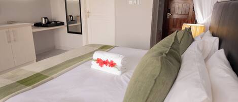 A neatly made bed with white linens and a green pillow, a bedside table with a lamp, and a wooden door in the background.