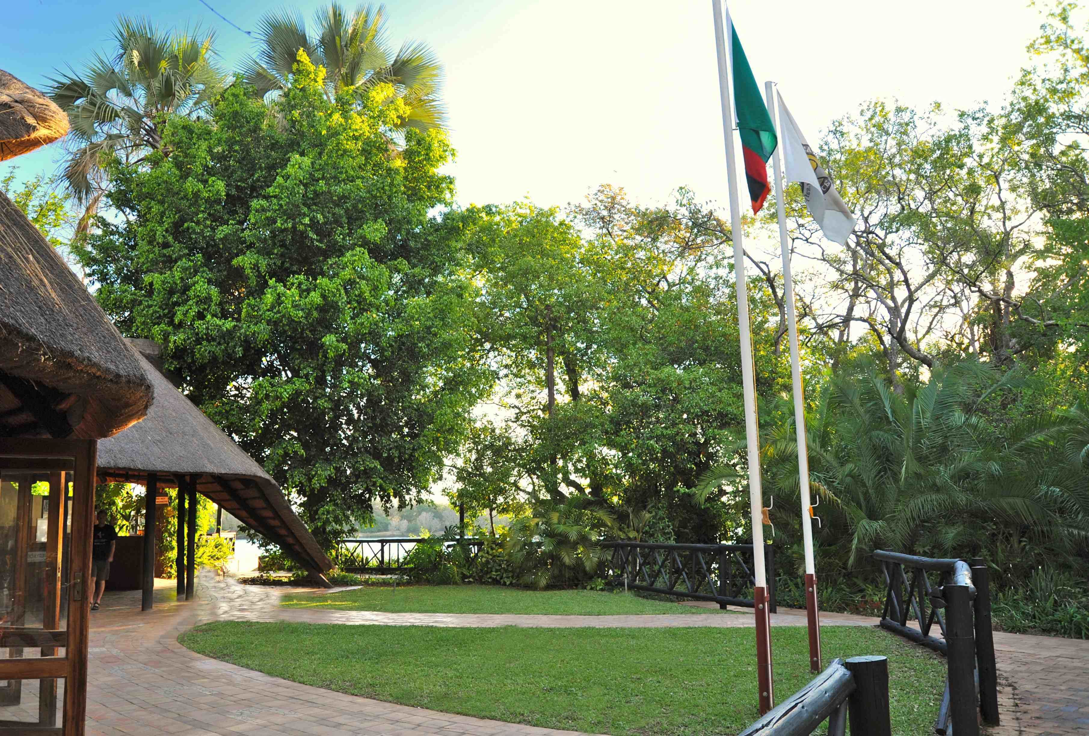 A thatched-roof pavilion, a flagpole with a flag, and a pathway surrounded by lush greenery.