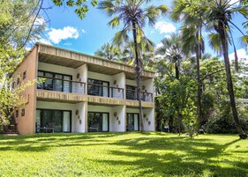 Un edificio de dos pisos con balcones, rodeado de exuberante vegetación y palmeras.