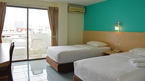 Een hotelkamer met twee bedden, een tafel, een stoel en uitzicht op de stad door een groot raam.