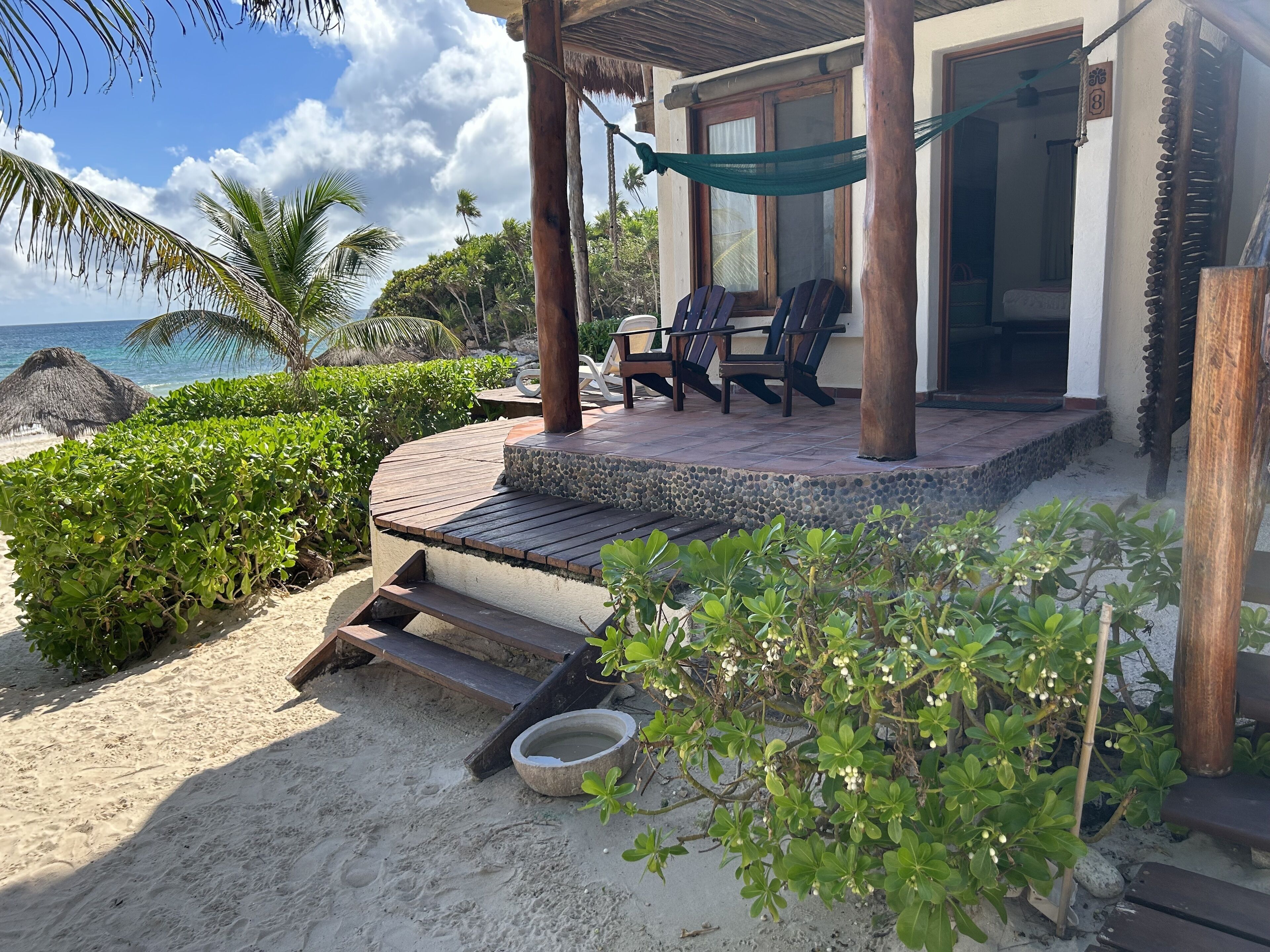 A beachside patio with wooden steps leading to a covered seating area with two chairs.
