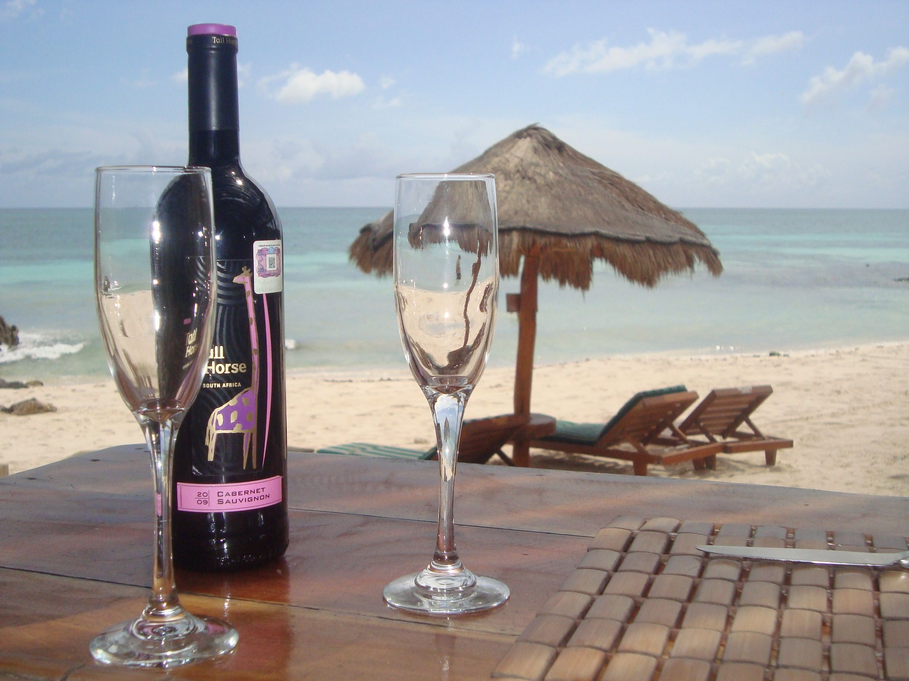 A bottle of wine and two glasses on a table with a beach view in the background.
