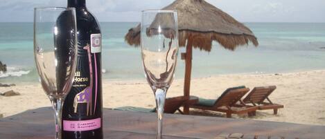 A bottle of wine and two glasses on a table with a beach view in the background.