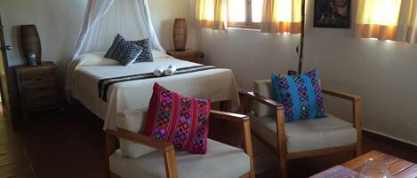 Quarto com cama, duas cadeiras de madeira, uma mesa e janela com cortinas.
