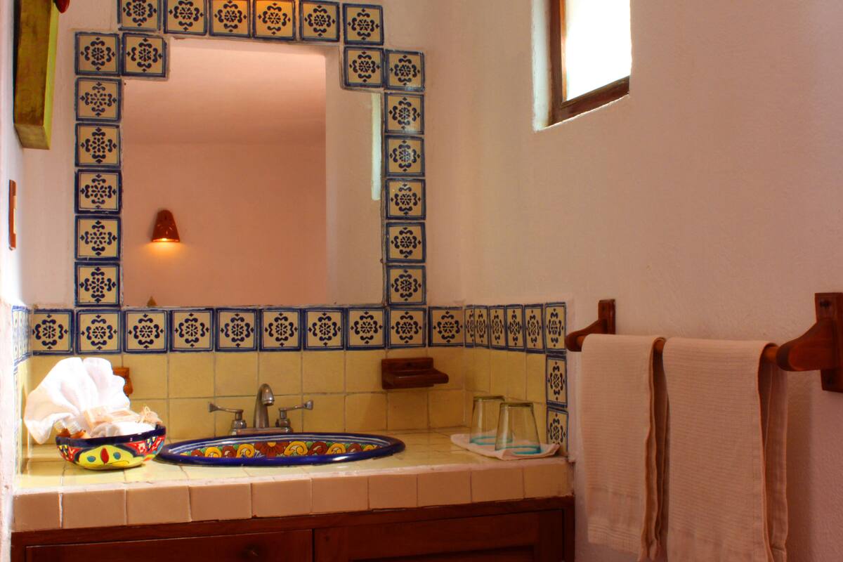 A bathroom with a tiled backsplash, a sink, a mirror, and a towel rack.