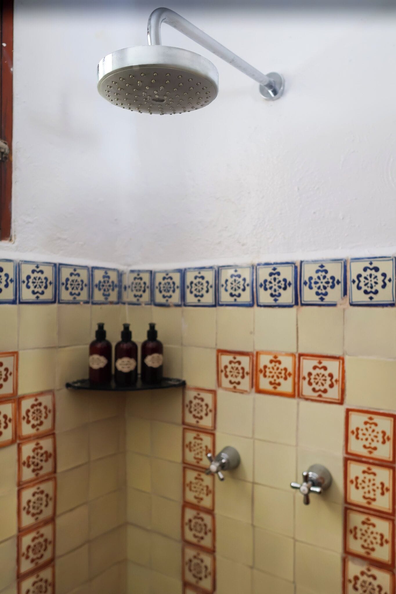 A shower with a handheld head, a shelf with bottles, and a tiled wall with a pattern.