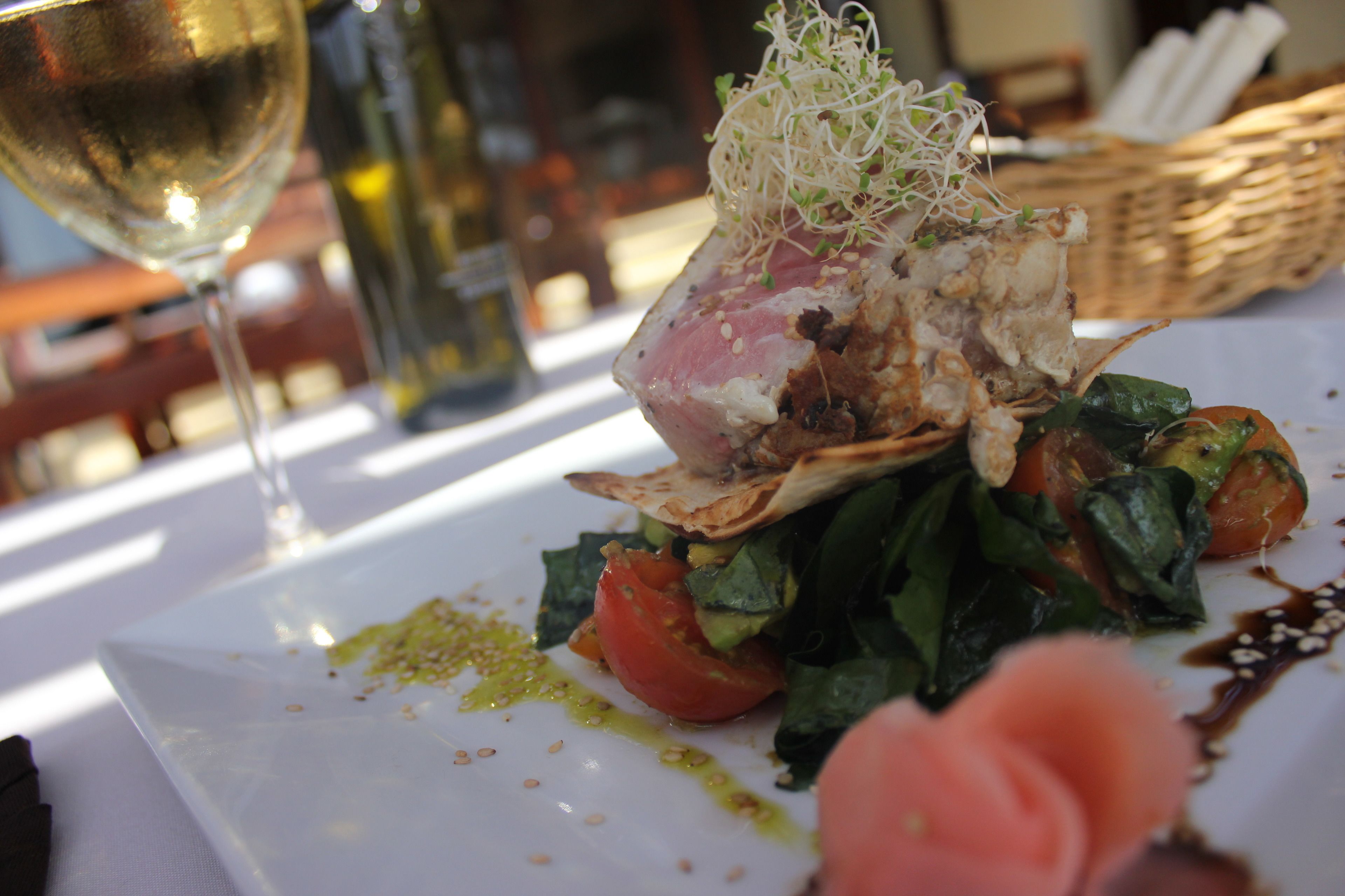 A plate of food with a glass of white wine and a bottle of wine in the background.