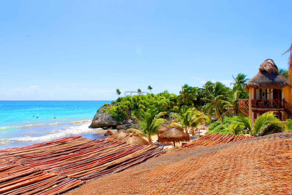 A beach with thatched-roof huts, palm trees, and a clear blue sky.