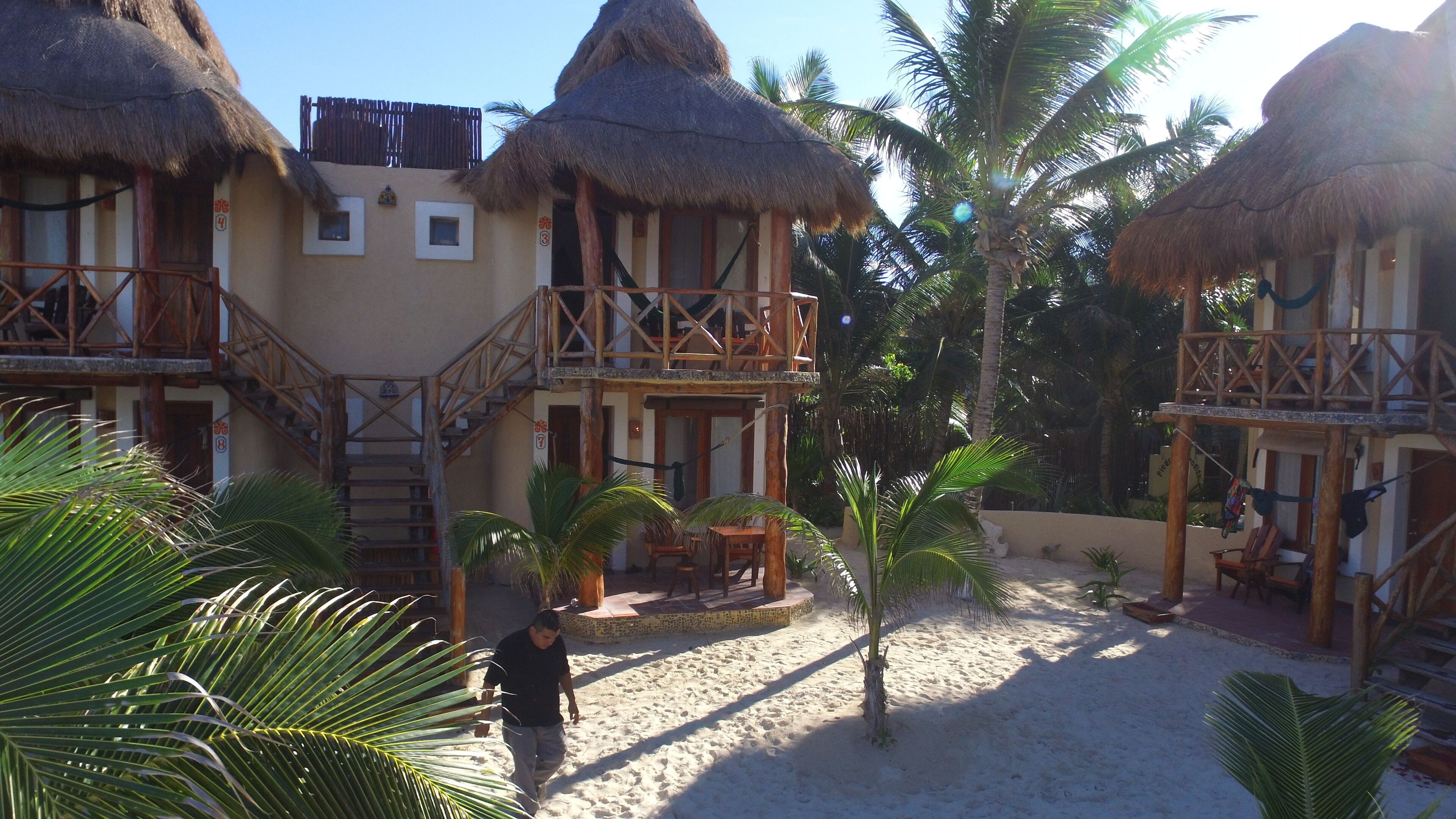 A resort with thatched-roof bungalows, a sandy courtyard, and palm trees.
