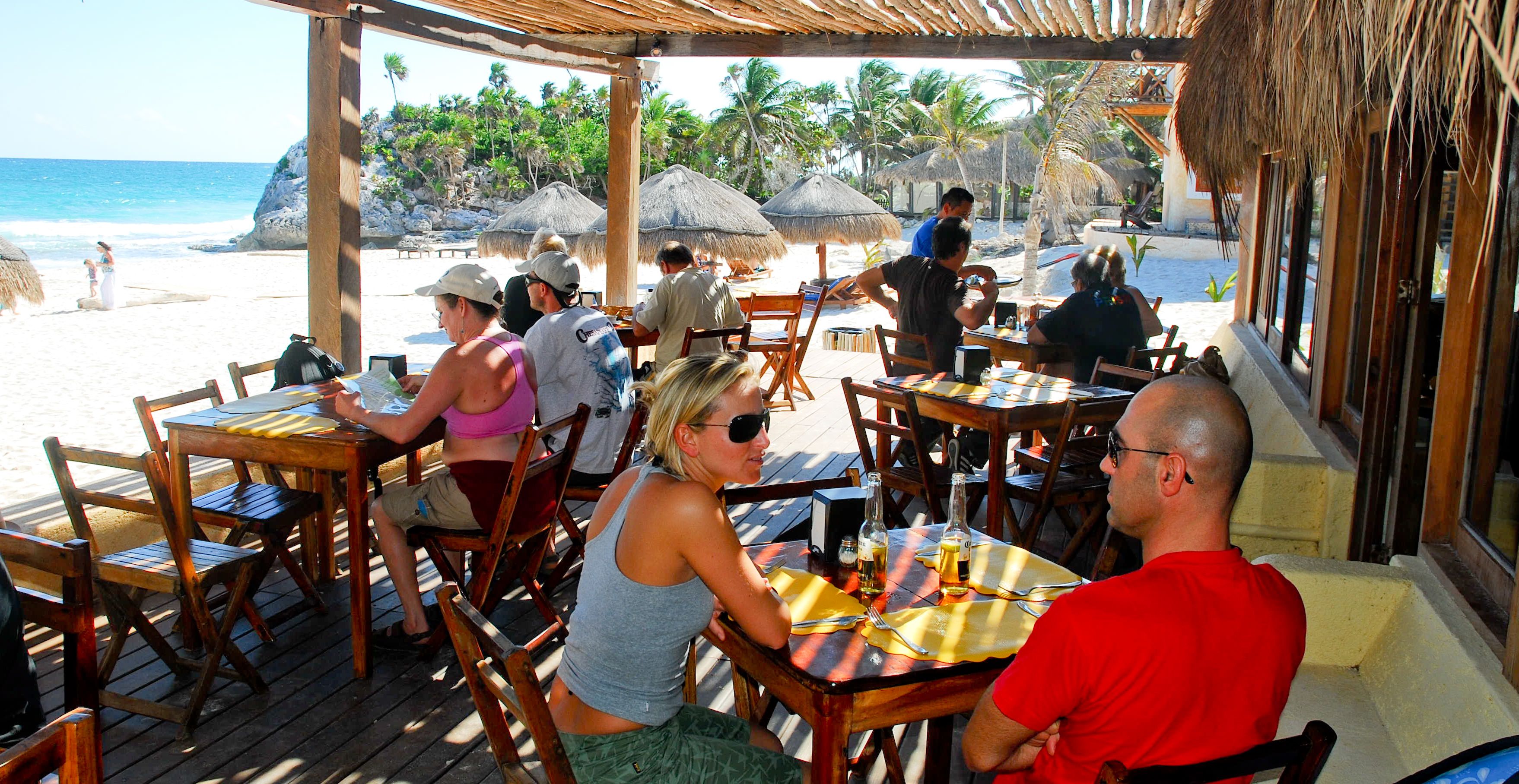 A beachside restaurant with wooden tables and chairs, overlooking the ocean.