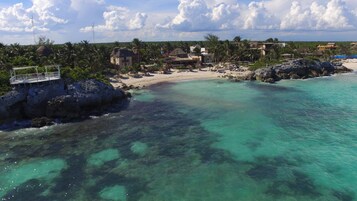 Um resort costeiro com uma praia de areia, águas turquesa cristalinas e estruturas com telhados de palha.