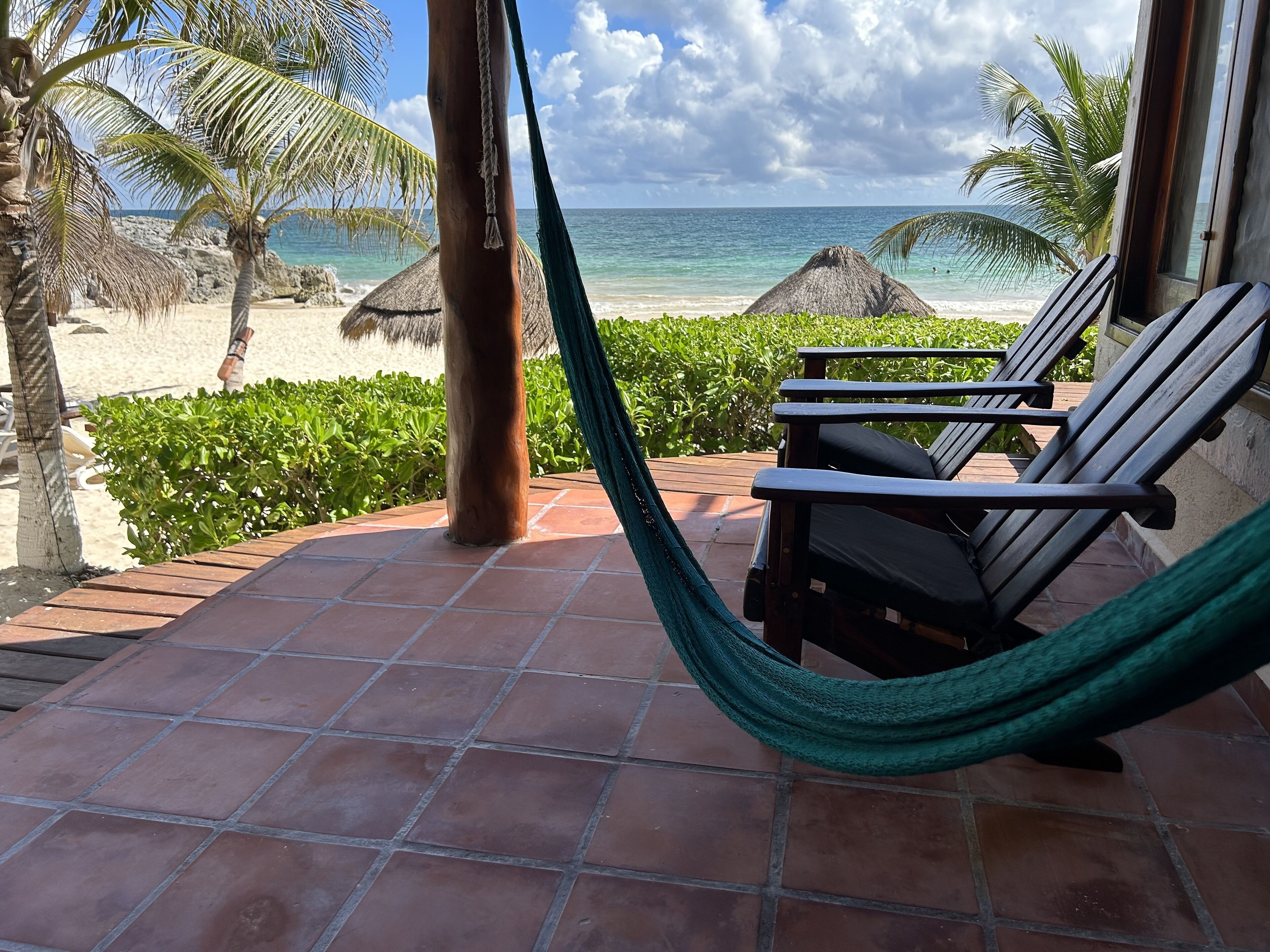 Une terrasse avec un hamac, des chaises en bois et une vue sur une plage et l’océan.